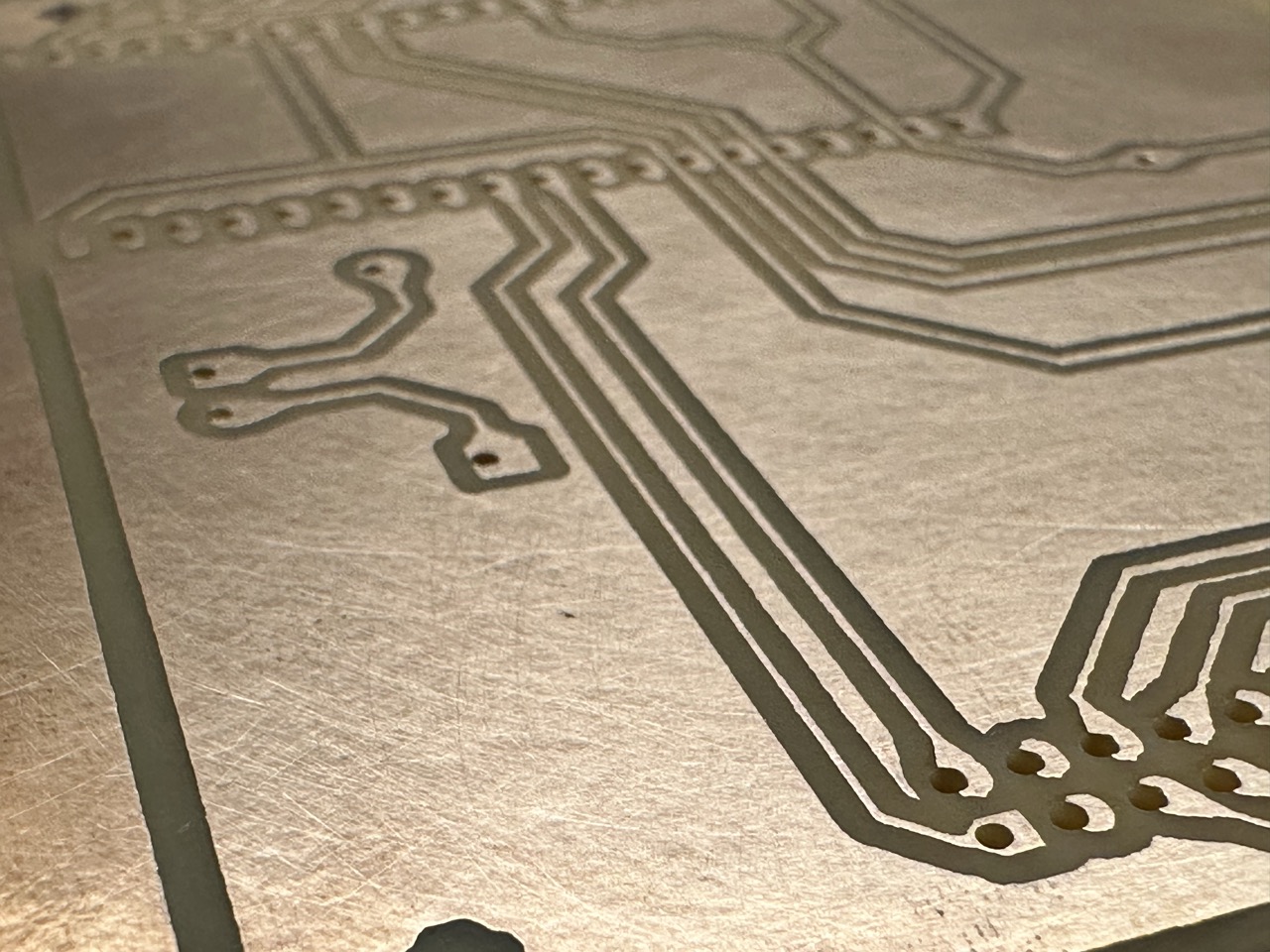 Close-up of a laser-etched copper PCB where several drilled holes sit off-center on their pads, some breaking into the pad edge.