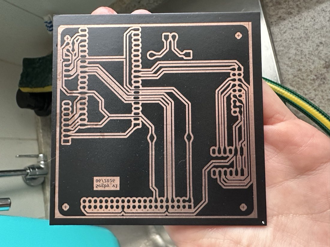 A hand holding an etched copper board over a sink, the trace pattern now in bright copper against the dark substrate where the copper has been etched away.