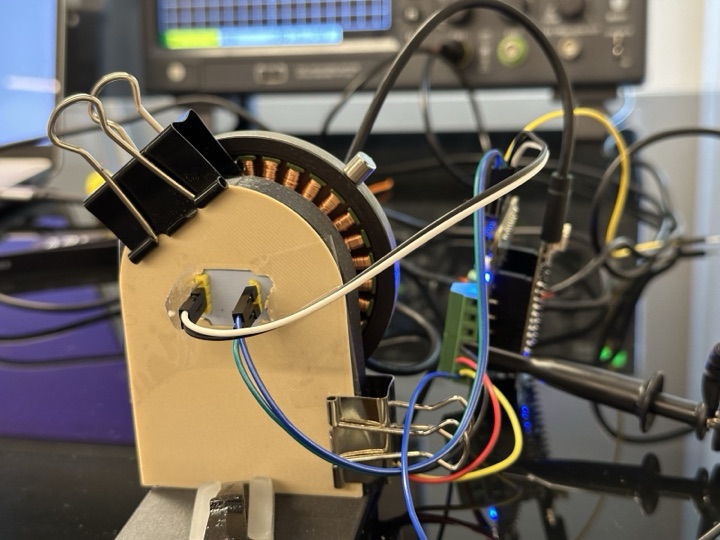 A 3D-printed plastic holder taped to the back of the motor stator, with an AS5600 magnetic-encoder breakout board mounted on it, ready to face a diametric magnet glued to the shaft.