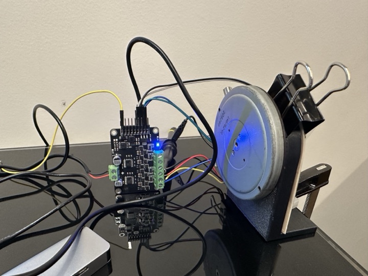The MKS Dual FOC v3.2 Plus board on the bench, blue power LED lit, three coloured phase wires running to the floppy spindle motor on the right. The motor disc is slightly blurred from rotation.